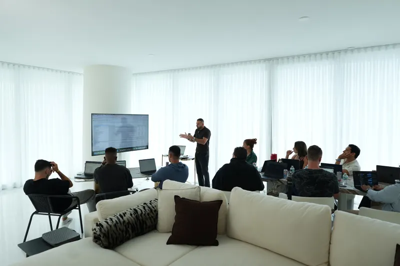 A host walks a small room of agency owners through a spreadsheet on a big screen while they follow along on laptops